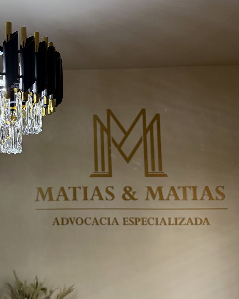 Parede da recepção com o logo dourado Matias & Matias e lustre de cristal